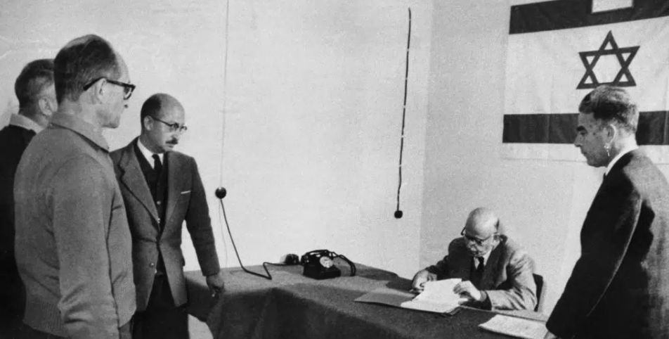 Toto je prvá fotografia Adolfa Eichmanna z roku 1961, ktorú urobil policajný fotograf vo väzení na tajnom mieste v Izraeli. Druhý vľavo je izraelský policajt A. Less, druhý vpravo je izraelský právnik A. Bach a vpravo policajt E. Hoffstetter. Zdroj: IZRAELSKÁ POLÍCIA 
